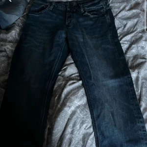 Mörkblå jeansbyxor - Säljer ett par klassiska mörkblå jeans med raka ben och fem fickor. Jeansen har normal passform och är tillverkade i denim. Perfekta till vardags och enkla att matcha med olika stilar.