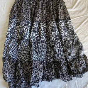 Svart och vit mönstrad kjol från Lindex - Säljer en svart och vit långkjol från Lindex med flera olika blommiga mönster i lager på lager. Kjolen har en luftig och flowy känsla, perfekt för dig som gillar bohemisk stil.