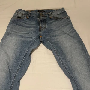 Grim Tim från Nudie Jeans - Säljer ett par klassiska blå jeans från Nudie Jeans i modellen W32 L32. Jeansen har en slim tapered passform, raka ben och snygga orange sömmar. Perfekta till vardags och passar till det mesta. Otroligt snygga med skick på 9/10. Stryka kan behövas dock då de har legat i garderoben länge 