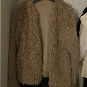 Beige teddyjacka - Säljer en beige teddyjacka med fluffig och mjuk yta från Gina tricot.. Jackan har lång ärm och är öppen framtill utan synliga knappar eller dragkedja. Perfekt för dig som vill ha en trendig och mysig look.