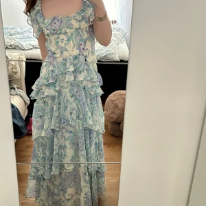 Blommig långklänning - Romantisk ljusblå långklänning med blommigt mönster. Den är klädd i volanger vilket gör den så rörlig och fin💕 Den är öppen i ryggen och perfekt som bröllopsgäst eller som balklänning. Jag är 169 och den är perfekt i längden på mig. Klänning n är 34 men är liten i storleken då jag har 36/38 😊Använd endast en gång!