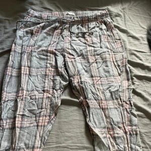 Rutiga mjukisbyxor med dragsko - Superbekväma mjukisbyxor i grått och rosa rutigt mönster. Byxorna har elastisk midja med dragsko för extra komfort. Perfekta för slappa dagar hemma eller när du vill vara extra cozy.