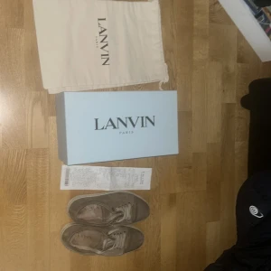 Beige sneakers från Lanvin - Säljer ett par beige sneakers från Lanvin med rund tå och platt sula. Skorna har snörning och är tillverkade i skinn. Klassisk och stilren design med ljusa skosnören och diskreta detaljer. Med kvitto 🧾!