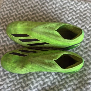 Addidas crazy fast elite  - Säljer ett par gröna fotbollsskor från Adidas med svarta ränder på sidorna. Skorna har en strömlinjeformad design utan snörning och är tillverkade i syntetmaterial. Perfekta för dig som vill sticka ut på planen!