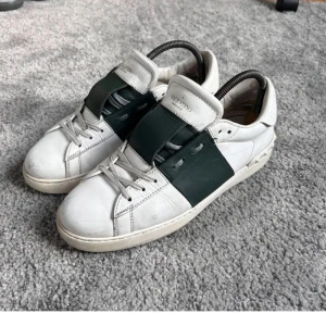 Valentino Open sneakers i vitt och grönt - Säljer ett par snygga Valentino Open sneakers i vitt skinn med en grön bred rem över mitten. Klassisk rund tå och platt sula. Perfekta för dig som gillar stilrena och exklusiva sneakers med en twist.