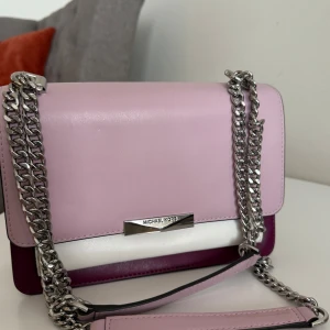 Michael Kors axelväska i rosa och vinrött skinn - Säljer en snygg axel och handväska från Michael Kors i rosa, vinrött och vitt skinn. Perfekt för dig som vill ha en stilren och trendig accessoar. Använt några gånger och är felfri 