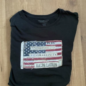  t-shirt från Ralph Lauren - Säljer en mörkgrön t-shirt från Ralph Lauren med ett coolt tryck av en sliten amerikansk flagga och texten 'Denim & Supply'. Perfekt för en avslappnad stil. Tillverkad i 100% bomull. Mellan 300kr-400kr funkar!