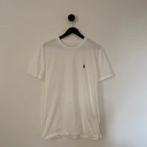 Vit t-shirt från Ralph Lauren - Klassisk vit t-shirt från Ralph Lauren med liten broderad logga i mörkblått på bröstet. T-shirten har rund hals och korta ärmar, perfekt för en clean och stilren look. S men är stor i storlek. 
