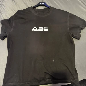 Svart t-shite,Speciell från A36,Man kan inte köpa dom,Jag fick den från honom. - Cool svart t-shirt med tryck av 'A36' på framsidan och ett futuristiskt planetmotiv på baksidan. Perfekt för dig som gillar unika och stilrena plagg.