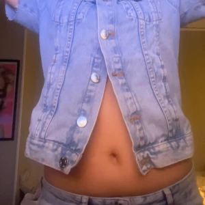 Ljusblå jeansjacka - Säljer en ljusblå jeansjacka med korta ärmar och knappar framtill. Jackan har en klassisk krage och två bröstfickor med knappdetaljer. Perfekt för en avslappnad stil.