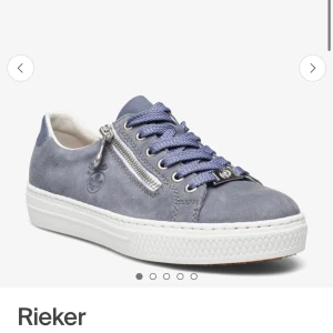 Oanvända Blå sneakers från Rieker med dragkedja - HELT NYA, ALDRIG ANVÄNDA. KÖPTA FÖR 850kr, SÄLJER FÖR 700kr.Snygga blå sneakers från Rieker i mocka med vita sulor. Skorna har både snörning och en dekorativ dragkedja på sidan samt en diskret logga. Perfekta för en avslappnad och trendig stil.