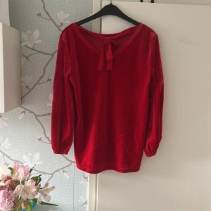 Röd sammetstopp från Hampton Republic - Snygg röd sammetstopp från Hampton Republic med en dekorativ knytning i nacken. Toppen har långa ärmar och en mjuk, glansig finish som ger en lyxig känsla. Perfekt för att lägga till en touch av elegans till din outfit.