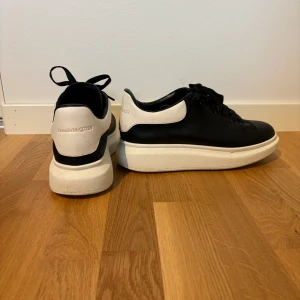 Svarta sneakers från Alexander McQueen - Säljer ett par svarta sneakers från Alexander McQueen med vit häl och tjock vit sula. Skorna har snörning och rund tå, klassisk design och är tillverkade i skinn. Perfekta för dig som gillar stilrena och trendiga sneakers. De är nytvättade. Kommer med dustbag.