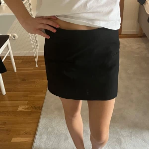 Svart minikjol från Zara - Säljer en svart minikjol från Zara med enkel och stilren design. Kjolen har två diskreta fickor framtill och är sydd i ett slätt material som ger en klassisk look. Perfekt att matcha med olika toppar för en trendig outfit.