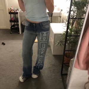 Blå jeans med tryck från SHEIN - Säljer ett par blå jeans från SHEIN i storlek XS. Byxorna har texten HONEY längs benet.