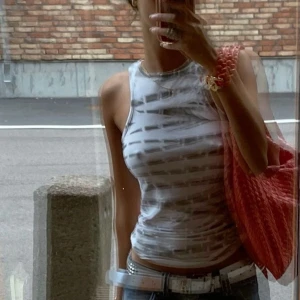 Vit och grå randig linnetopp - Säljer en stilren vit och grå randig linnetopp. Toppen är ärmlös och har en tight passform, perfekt för varma dagar. Den är enkel att matcha med olika outfits och accessoarer.