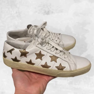 Saint Laurent skor vita - Skohylla rensning. •Saint Laurent SL/01 sneakers vita med guldiga stjärnor. Skick: 7-8/10, mycket varsamt använda! Vanligt bruks slitage som creases vid tån annars inga skador! Storlek: 40, fits 40-41. Vid köp medföljer: Original Box & YSL kort.. Självklart är skorna äkta! Nypris: 7 000 kr~.  Hör av dig vid frågor eller funderingar, mvh Oliver;)