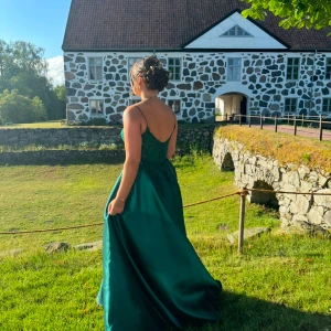Grön balklänning - Elegant grön långklänning med smala axelband och vackert spetsliv. Kjolen är i ett glansigt material som faller snyggt och ger en lyxig känsla. Perfekt för bal eller fest. Klänningen har öppen rygg och markerad midja. Använd en gång och är kemtvättad. Klänningen saknar storleksanvisning, men skulle säga att den passar storlek 38. Jag är 173 cm och hade klackar på 4 cm och då var den lite lång för mig, men det funkade. Nypris 4000 kr.