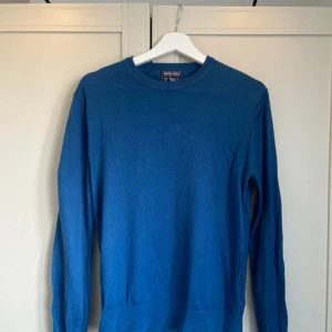 Blå bomullströja från Woolrich - Säljer en stilren blå tröja från Woolrich i 100% bomull. Tröjan har rund halsringning och långa ärmar, perfekt för en enkel och klassisk look. Passformen är normal och materialet känns mjukt mot huden.