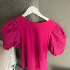 Rosa topp med puffärmar - Säljer en snygg rosa topp med stora puffärmar. Toppen har rund halsringning och är tillverkad i ett mjukt material som känns bekvämt mot huden. Perfekt för dig som vill sticka ut med en färgglad och trendig look.