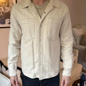 Beige overshirt med knappar - Stilren jacka/overshirt perfekt nu inför vår/sommar. Personen på bilden är 184cm