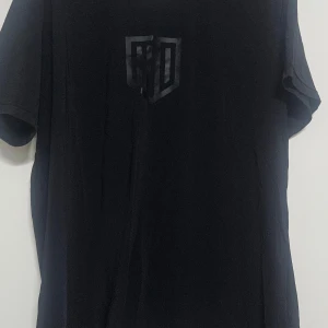 Svart t-shirt från Maya Delorez - Snygg svart t-shirt från Maya Delorez med ett diskret tryck på bröstet och tre horisontella linjer på ryggen. Perfekt för en stilren look. Tillverkad i ett bekvämt material.