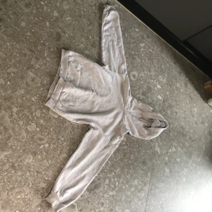 Ljusgrå hoodie från H&M - Mysig ljusgrå hoodie från H&M med klassisk huva och känguruficka framtill. Perfekt för en avslappnad stil och enkel att matcha med det mesta. Mjuk bomullskänsla och ribbade muddar vid ärmslut och nederkant.