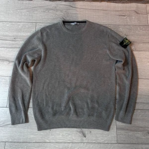 Grå stickad tröja från Stone Island - Säljer en grå stickad tröja från Stone Island i 100% bomull. Tröjan har rund halsringning, långa ärmar och klassisk Stone Island-logga på ärmen. Perfekt för dig som gillar stilrena och tidlösa plagg.