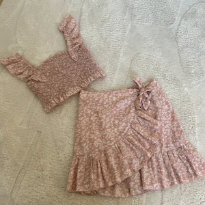 Rosa blommig omlottkjol med volang - Charmig rosa omlottkjol med blommönster och volangdetaljer. Kjolen har en knytning i sidan och är perfekt för en somrig look.