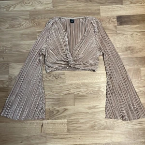 Beige randig blus från Shein - Säljer en beige randig blus från Shein med långa vida ärmar och en knytdetalj framtill. Blusen har en v-ringad design och är croppad, vilket ger en trendig look. Perfekt för att lyfta din outfit! Är jätte söt att ha på linnen osv!