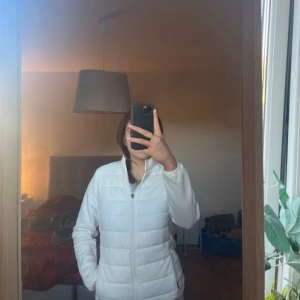 Vit jacka från Four-D - Säljer en stilren vit jacka från Four-D. Jackan har en dragkedja framtill och är tillverkad i ett vindtätt material. Perfekt för kyliga dagar med sin långa ärm och bekväma passform. Enkelt och snyggt val för alla tillfällen.