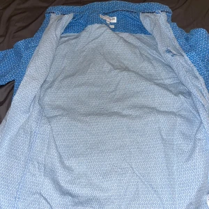 Blå mönstrad skjorta från U.S. Polo Assn. - Säljer en blå slim fit skjorta från U.S. Polo Assn. i storlek XS. Skjortan har ett småblommigt mönster och klassisk krage. Perfekt för dig som gillar en smalare passform och stilren design. Knappar framtill. Helt äkta.