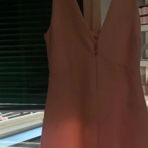 Ljusrosa ärmlös klänning med djup v-ringning zara  - Säljer en ljusrosa klänning med djup v-ringning och dekorativa knappar framtill. Klänningen är ärmlös och har en elegant, enkel design som passar perfekt till sommarens tillfällen.