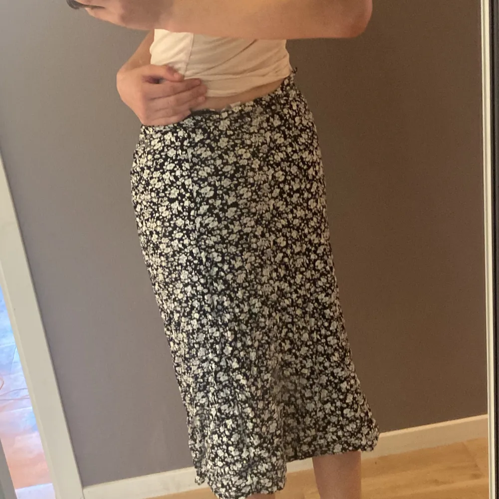Säljer en svart midilång kjol med vitt blommönster från New Yorker. Kjolen har en slits framtill och är i ett lätt, flowy material som känns skönt mot huden. Dragkedja på sidan i midjan. Knappt använd, pris går att diskutera. Hameet.