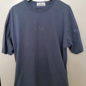 Blå t-shirt från Stone Island - Snygg blå t-shirt från Stone Island med diskret broderad logga på bröstet. Klassisk rund halsringning och avslappnad passform. Perfekt till jeans eller shorts för en clean look.