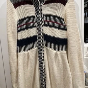 Stickad cardigan kofta från Bondelid - Snygg stickad cardigan kofta från Bondelid med huva och coolt mönster i beige, marinblått, vinrött och grått. Jackan har knappar framtill, långa ärmar och en skön loose fit. Perfekt för lager-på-lager och chillare dagar. Den är i jätte bra skick 