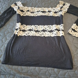 Svart spetsblus från Intimissimi - Supersnygg svart blus från Intimissimi med långa ärmar och breda, krämvita spetsdetaljer över axlar, ärmslut och midja. Blusen har en figurnära passform och romantiska spetsinslag som ger en unik look. Perfekt för dig som vill sticka ut lite extra. Den är i väldigt fin skick. Storlek M. 