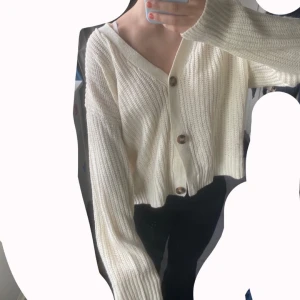 Krämvit stickad kofta Brave Soul - Supermysig krämvit stickad kofta från Brave Soul med v-ringning och stora bruna knappar framtill. Koftan är croppad med lång ärm och har en chunky ribbad struktur som ger en chill vibe. Perfekt att slänga över ett linne eller t-shirt.