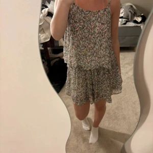 Blommig tvådelars sett från Clockhouse - Supersöt två delar sett från Clockhouse Elements Collection med blommigt mönster i rosa, vit, gul och grön. Den har tunna axelband, flowig passform och volangig kjol. Perfekt för varma dagar och ger en fräsch sommarkänsla.