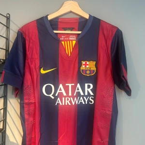 FC Barcelona Neymar Jr matchtröja - Säljer en officiell FC Barcelona matchtröja från Nike med Neymar Jr och nummer 11 på ryggen. Tröjan har breda blå och röda ränder, gula detaljer och klubbmärke på bröstet. Tillverkad i lätt och ventilerande Dri-FIT-material, perfekt för fotbollsälskare. Helt ny med tagg en replika