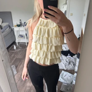 Gul volang halterneck topp - Supersöt ljusgul linnetopp med flera lager volanger framtill och halterneck med knyt i nacken. Toppen är ärmlös och croppad, perfekt för en trendig look. Från Gina Tricot som är slutsåld på hemsidan😊
