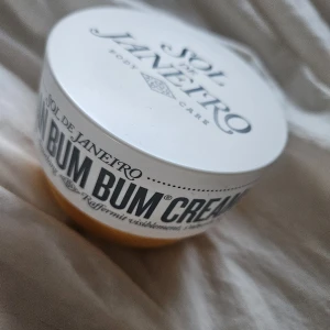 Sol de Janeiro Bum Bum Cream - Ikonisk Bum Bum Cream från Sol de Janeiro i en rund, gul plastburk med vitt lock. Krämen är ljusgul och har en krämig konsistens. Doftar tropiskt och ger huden en silkeslen känsla. Perfekt för dig som vill ha glow och mjuk hud. Cirka 90% kvar, förvarad svalt och mörkt, inköpt 5 mån sedan.