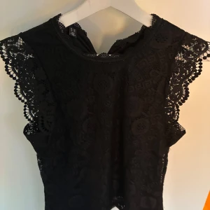 Svart spetsblus från Pieces  - Supersnygg svart blus från Pieces i storlek XS. Blusen är helt i spets med vackra detaljer och mönster, har ärmlös design med dekorativa spetskanter och rund halsringning. 🌟