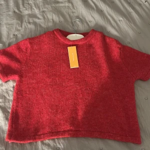 Röd stickad kortärmad topp - En röd stickad topp med lapparna kvar, storlek 146/152