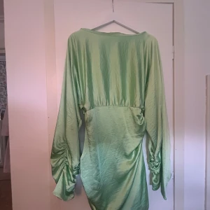 Grön satin-klänning NA-KD x Hanna Schönberg - Snygg ljusgrön kortklänning i satin från NA-KD x Hanna Schönberg. Klänningen har långa, vida ärmar med rynkade detaljer och markerad midja. 
