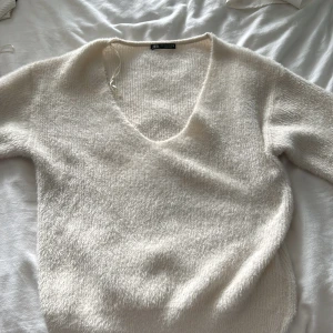 Vit stickad v-ringad tröja från Zara - Mysig vit stickad tröja från Zara i storlek S. Tröjan har en djup v-ringning och lång ärm, perfekt för lager-på-lager. Den fluffiga strukturen ger en soft och chill vibe, lätt att matcha med jeans eller kjol.