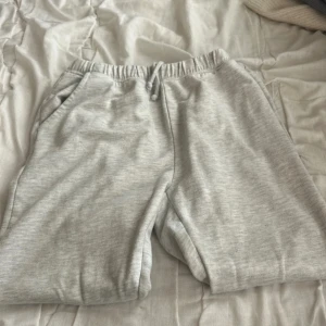 Gråa mjukis med snöre från lager 157 - Mysiga ljusgrå mjukisbyxor från lager 157 med elastisk midja och snörning. Mjukisbyxorna har två sidofickor och är tillverkade i mjuk bomullsmix. Perfekta för chill dagar eller träning. Enkel och clean look som passar till allt.