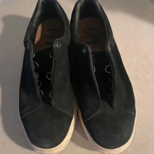 Svarta sneakers i mocka med vit sula - Stilrena svarta sneakers i mocka med lågt skaft och vit platt sula. I väldigt fint skick, bara använda vid enstaka tillfällen, så gott som nya. Storlek 41 men passar även en 39-40 som mig själv. 