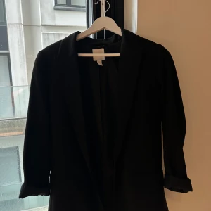Svart kavaj från H&M i XS - Stilren svart kavaj från H&M i storlek XS. Klassisk modell med slag och långa ärmar som kan vikas upp för en mer avslappnad look. Perfekt att matcha med jeans eller kostymbyxor för en snygg outfit.