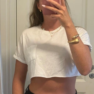 Vit croppad t-shirt med ficka - Säljer en vit croppad t-shirt med korta ärmar och en liten bröstficka. T-shirten har en avslappnad passform och är gjord i mjuk bomull. Perfekt för en chill och trendig look.